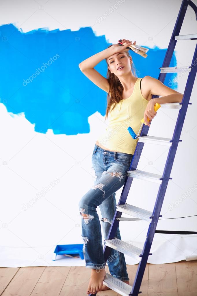 Happy beautiful young woman doing wall painting, standing near ladder