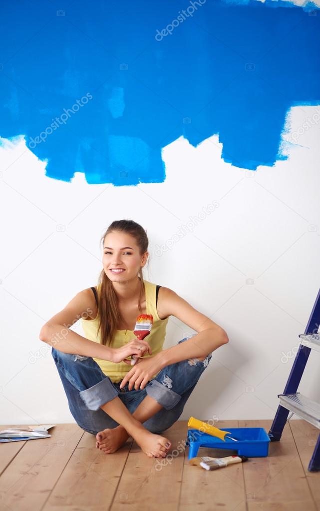 Portrait of female painter sitting on floor near wall after painting.