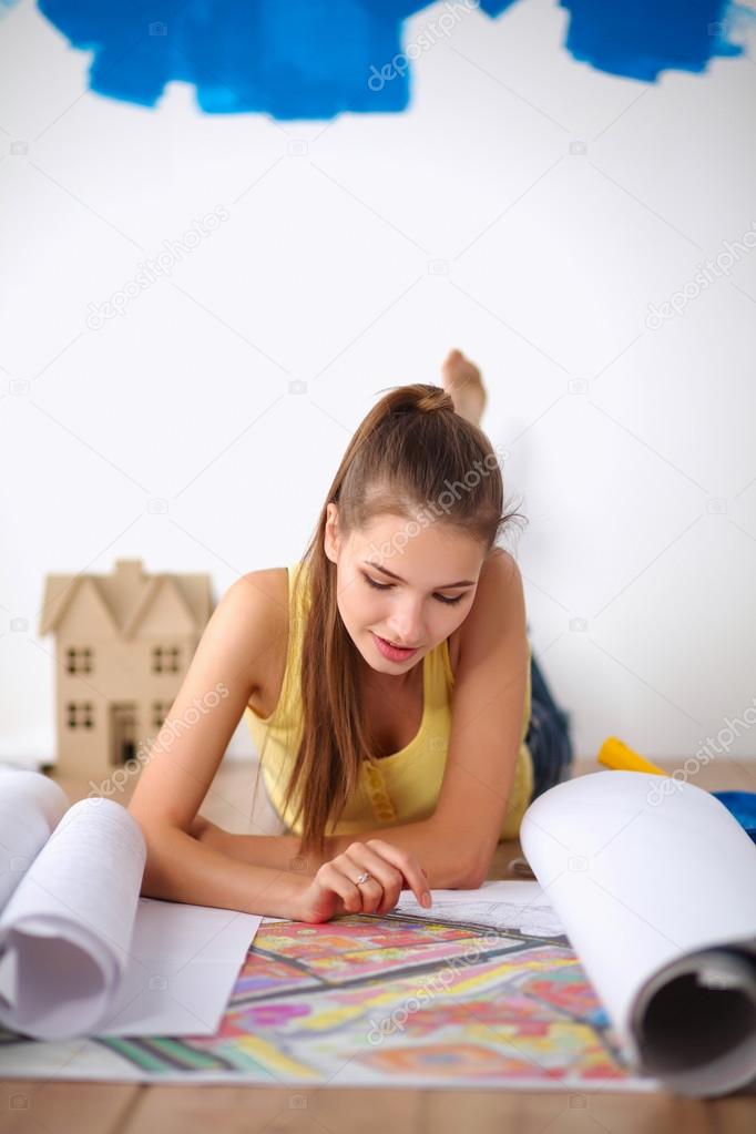 Young woman lying on the floor and looking at blueprint of new house