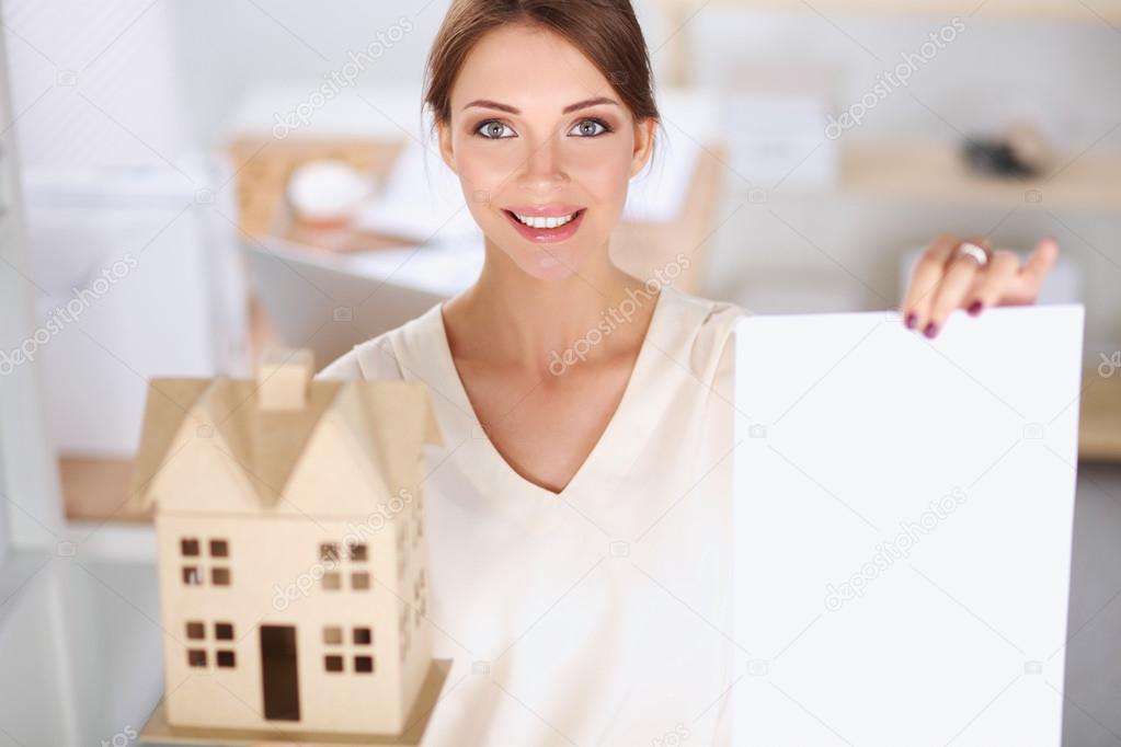 Portrait of female architect holding a little house, standing in office, isolated