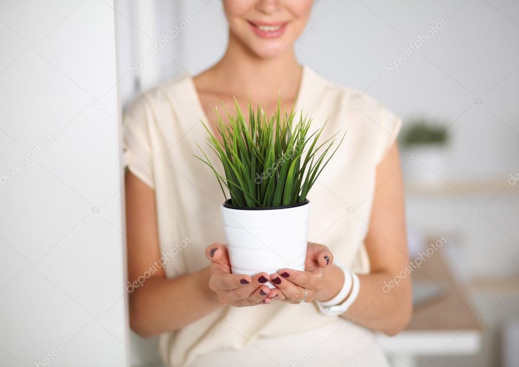 Beautiful woman holding pot with a plant, standing at home