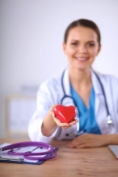 Jovem médico com símbolo de coração vermelho sentado na mesa isolado — Fotografia de Stock