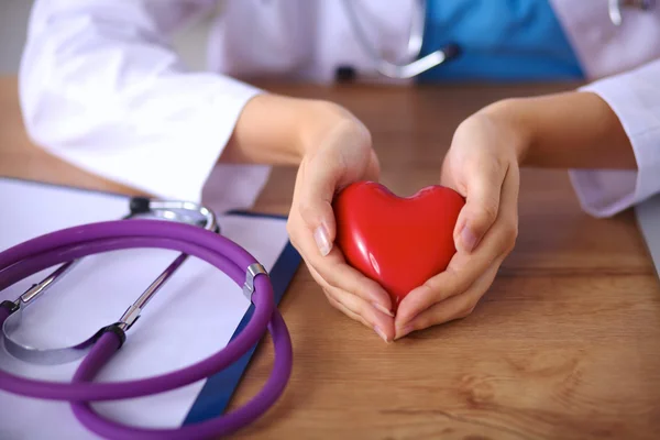 Joven médico con el símbolo del corazón rojo sentado en el escritorio aislado — Foto de Stock