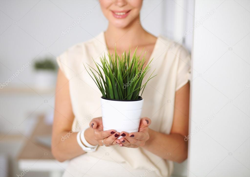 Beautiful woman holding pot with a plant, standing at home