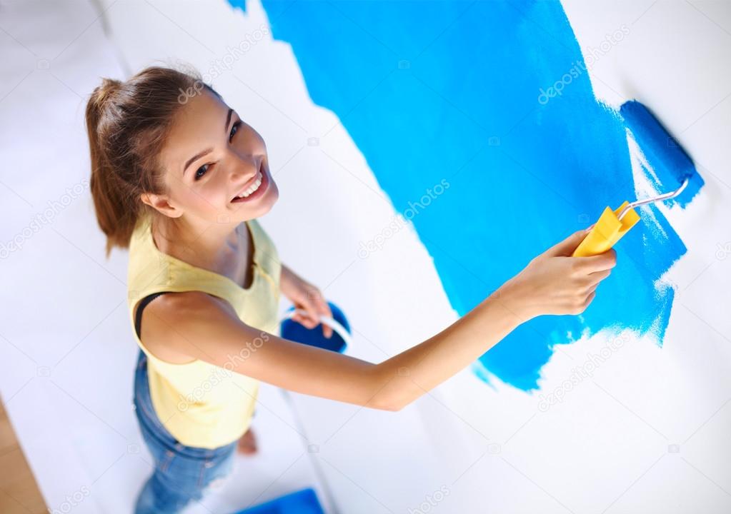 Happy beautiful young woman doing wall painting, standing on la