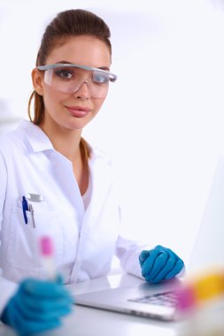 Kadın araştırmacının etrafı ilaç şişeleri ve mataralarla çevrili.