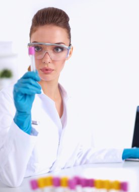 Kadın araştırmacı, beyaz arka planda izole edilmiş ilaç şişeleri ve mataralarla çevrili.