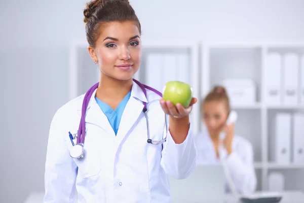 Ženský lékař ruka drží zelené jablko, stojící v úřadu — Stock fotografie