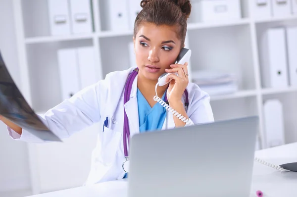 Médecin féminin regardant radiographie et parlant au téléphone dans le centre de diagnostic, assis au bureau — Photo