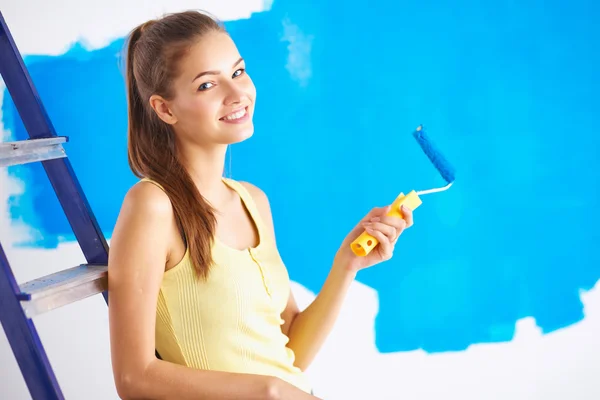 Gelukkig mooie jonge vrouw doet wandschildering, zittend op de ladder — Stockfoto