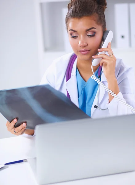 Médica olhando radiografia e falando por telefone no centro de diagnóstico, sentada na mesa — Fotografia de Stock