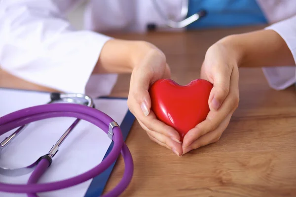 Joven médico con el símbolo del corazón rojo sentado en el escritorio aislado —  Fotos de Stock