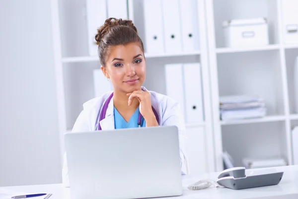 Female doctor sitting on the desk and working a laptop in hospital — Stock Photo, Image