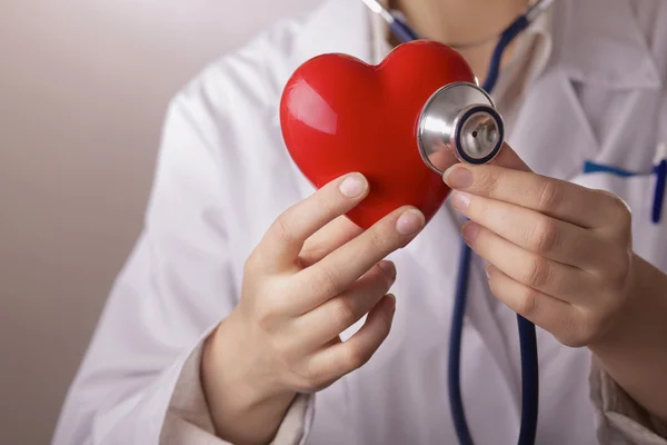 Un médecin avec stéthoscope examinant le cœur rouge, isolé sur fond gris — Photo