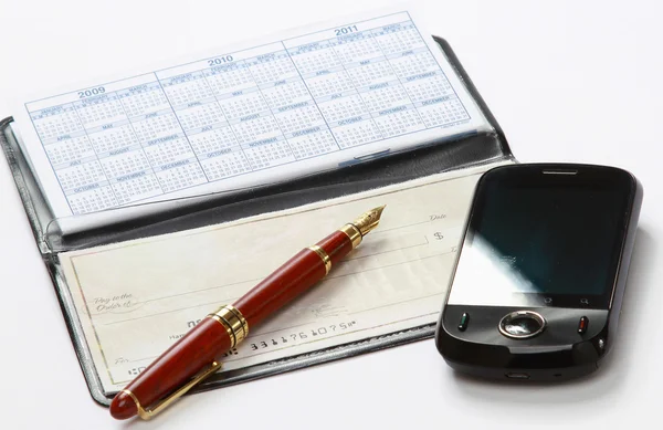 A pen and a mobile phone over a checkbook — Stock Photo, Image
