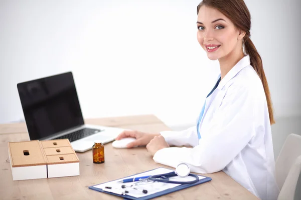 Hermosa joven sonriente doctora sentada en el escritorio y escribiendo. —  Fotos de Stock