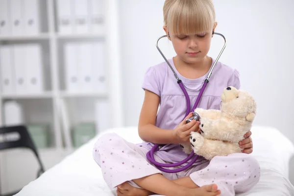 Niña está examinando su osito de peluche usando estetoscopio — Foto de Stock