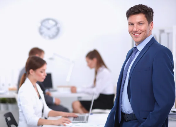 Erfolgreicher Geschäftsmann steht mit seinen Mitarbeitern im Hintergrund im Büro — Stockfoto