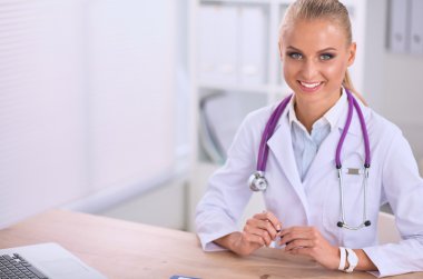 Güzel, genç, gülümseyen bayan doktor masada oturuyor ve yazıyor..