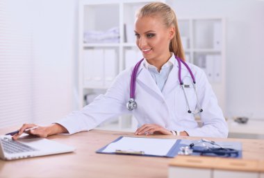 Güzel, genç, gülümseyen bayan doktor masada oturuyor ve yazıyor..