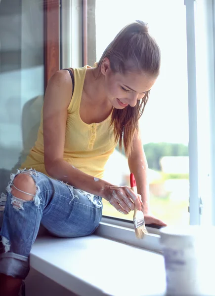 Mujer pintando la pared de un apartamento con un pincel cuidadosamente terminando alrededor del marco de la ventana —  Fotos de Stock