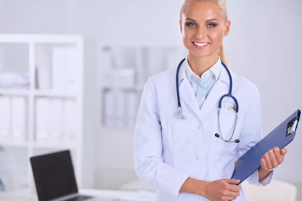 Médico sonriente con una carpeta en uniforme de pie en el hospital —  Fotos de Stock