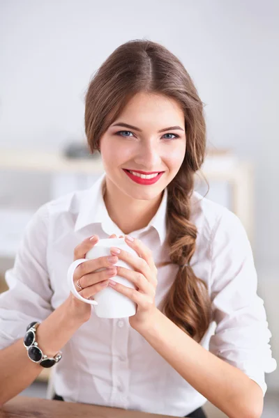 Joven mujer de negocios sentada en el escritorio con taza en la oficina — Foto de Stock