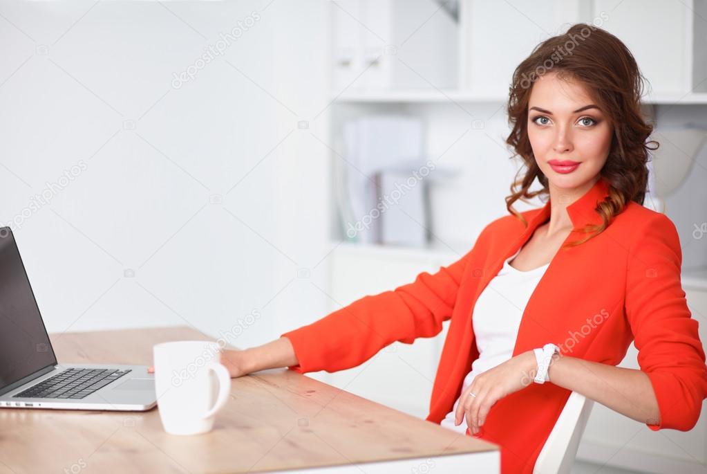 Attractive woman sitting at desk in office, working with laptop computer