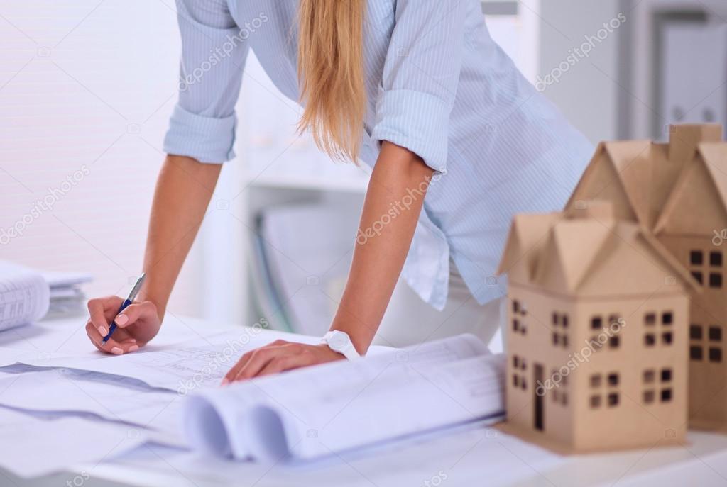 Portrait of female architect with blueprints at desk in office