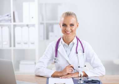 Güzel, genç, gülümseyen bayan doktor masada oturuyor ve yazıyor..