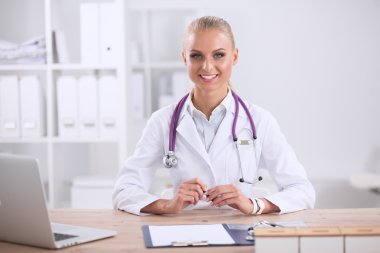 Güzel, genç, gülümseyen bayan doktor masada oturuyor ve yazıyor..