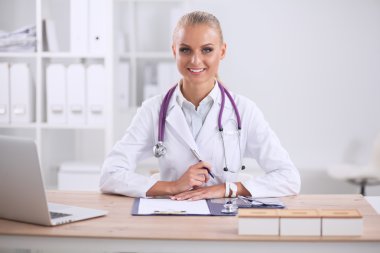 Güzel, genç, gülümseyen bayan doktor masada oturuyor ve yazıyor..