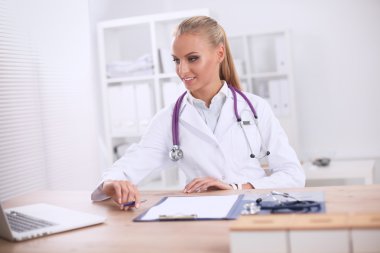 Güzel, genç, gülümseyen bayan doktor masada oturuyor ve yazıyor..