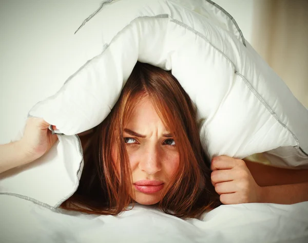 Weibchen liegt auf Bett und schließt ihre Ohren mit Kissen — Stockfoto