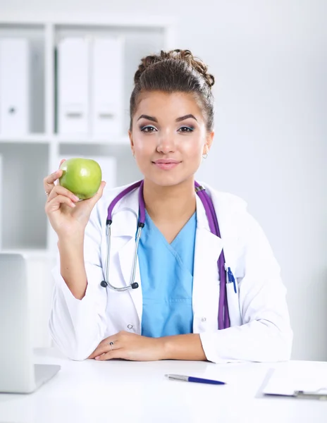 Mão médica feminina segurando uma maçã verde, sentada na mesa — Fotografia de Stock