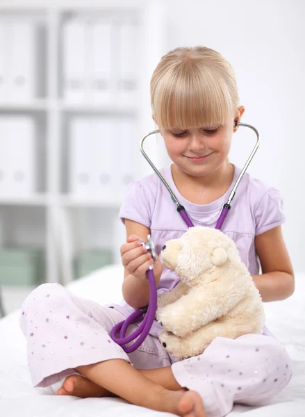 Klein meisje onderzoekt haar teddybeer met stethoscoop. — Stockfoto