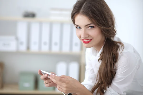 Zakenvrouw stuurt bericht met smartphone zittend op kantoor — Stockfoto