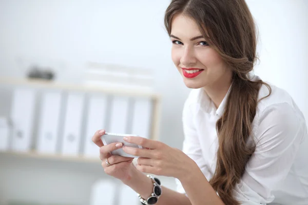 Businesswoman sending message with smartphone sitting in the office — Stock Photo, Image