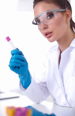 Kadın araştırmacı, beyaz arka planda izole edilmiş ilaç şişeleri ve mataralarla çevrili.