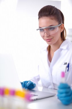 Kadın araştırmacı, beyaz arka planda izole edilmiş ilaç şişeleri ve mataralarla çevrili.