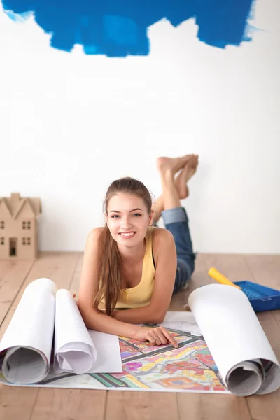 Mujer joven acostada en el suelo y mirando el plano de la nueva casa —  Fotos de Stock