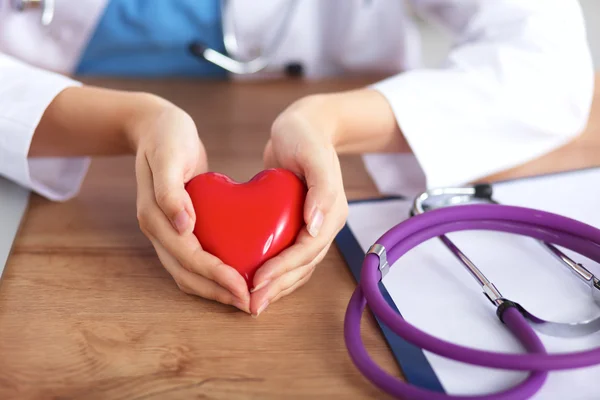 Ung läkare med röd hjärtsymbol sitter vid skrivbordet isolerad — Stockfoto