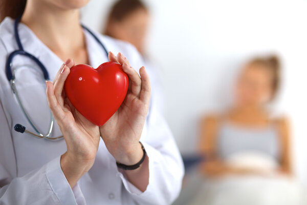 Young woman doctor holding a red heart, isolated on white background