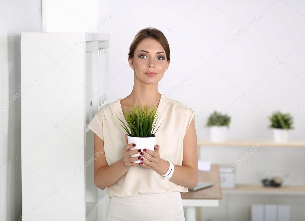 Beautiful woman holding pot with a plant, standing at home