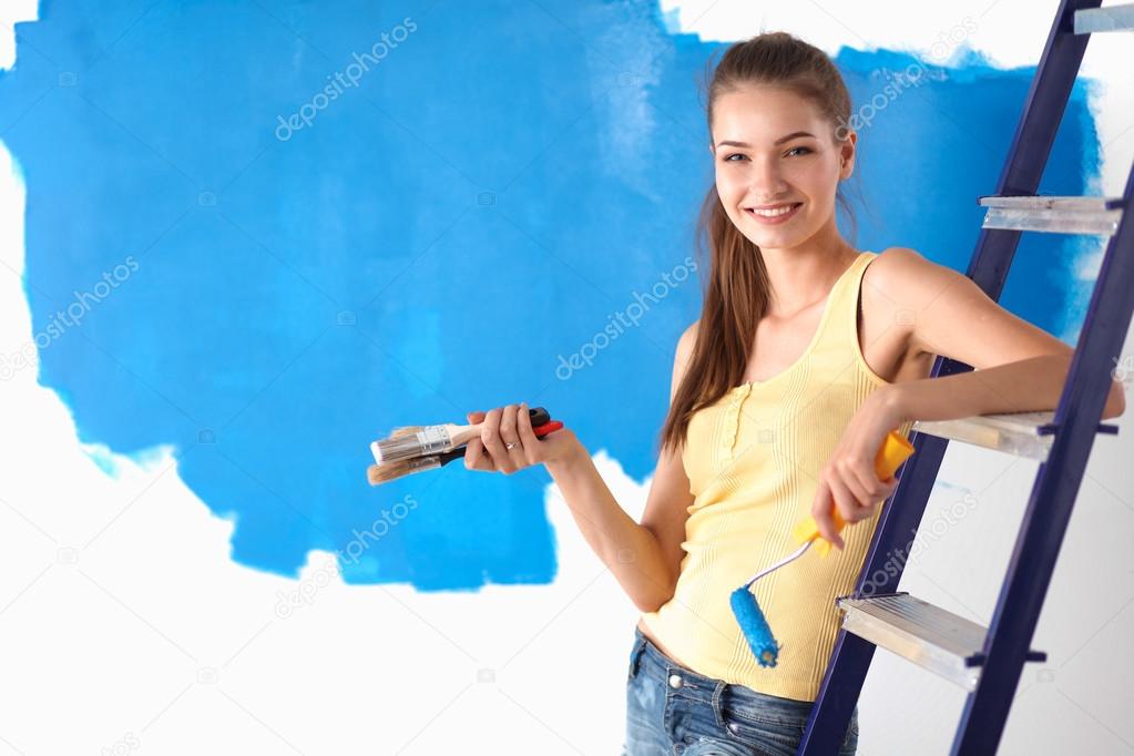 Happy beautiful young woman doing wall painting, sitting on ladder