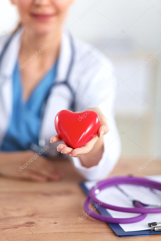 Young doctor with red heart symbol sitting at desk isolated