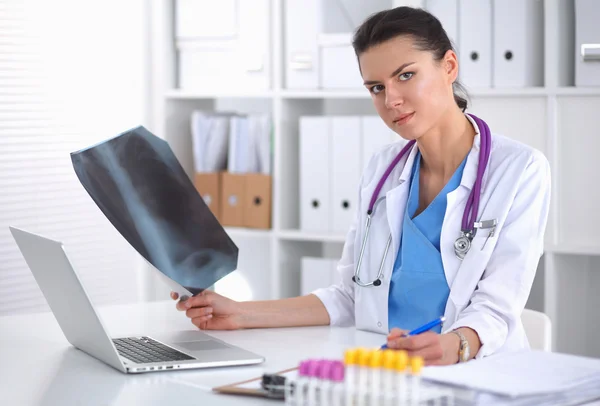 Jovem médica estudando radiografia sentada na mesa — Fotografia de Stock