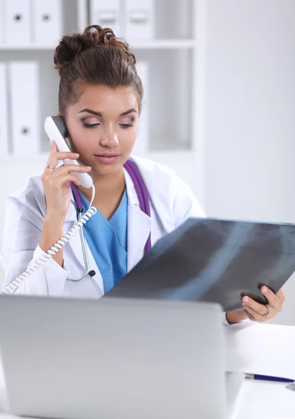 Vrouwelijke arts op zoek naar x-ray scan en praten over de telefoon in diagnostisch centrum, zittend aan het bureau — Stockfoto