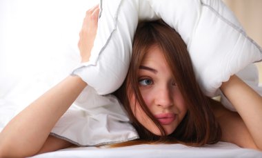 Kadın yatakta uzanıyor ve kulaklarını yastıkla kapatıyor.