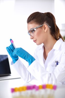 Kadın araştırmacı, beyaz arka planda izole edilmiş ilaç şişeleri ve mataralarla çevrili.